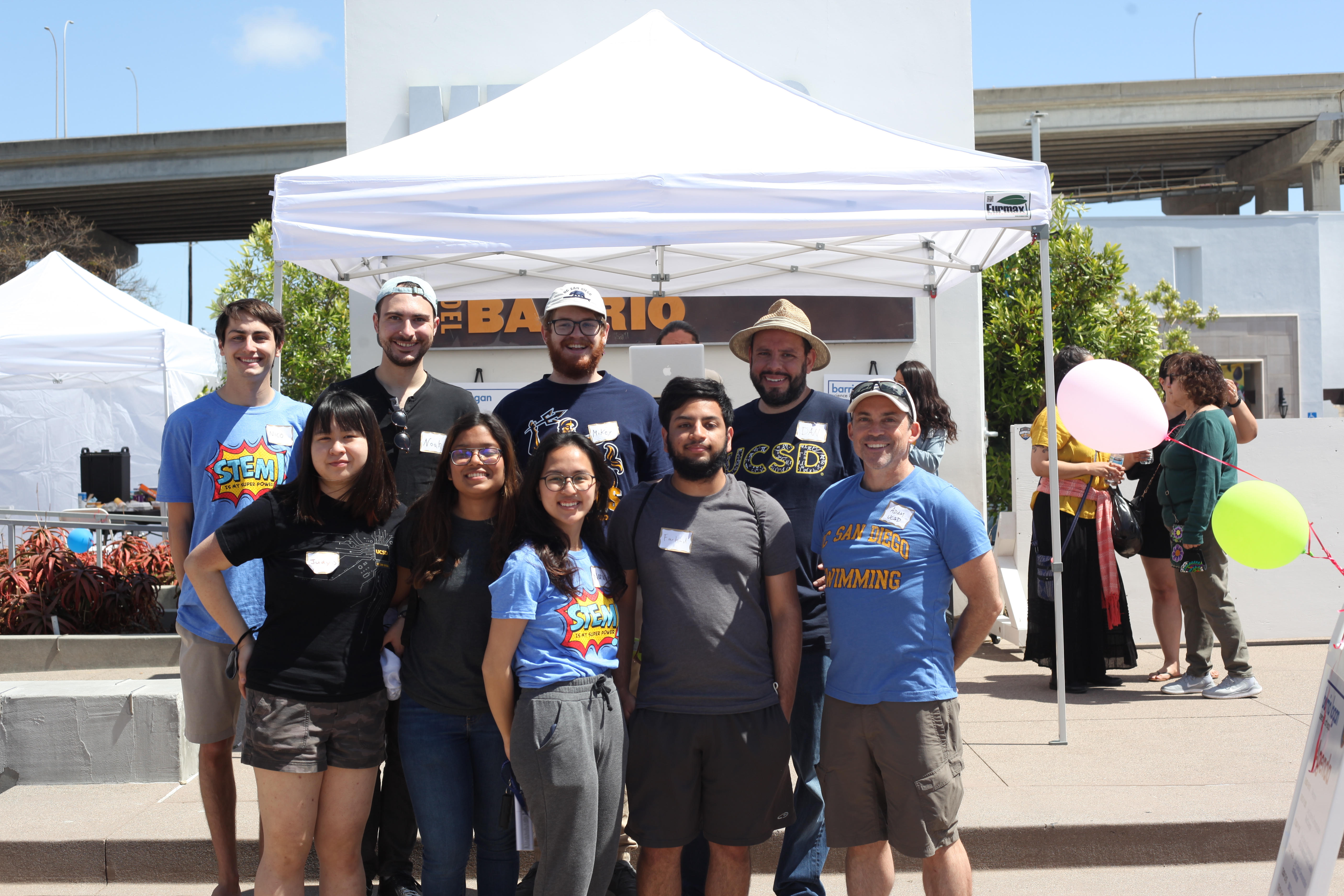 This image contains 9 people posing in front of a canopy. The people are representatives of UCSD at the 2022 SD STEAM Expo
